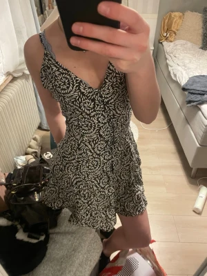 Svartvit blommig kortklänning - Snygg svartvit kortklänning med blommigt mönster och v-ringad hals. Klänningen har smala axelband och en lätt utställd kjol. Perfekt för varma dagar. Kommer från h&m och i storlek XS, den är aldrig använd och prislapp kvar. 