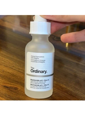 The Ordinary Niacinamide 10% + Zinc 1% - Transparent glasflaska med vit pipett från The Ordinary. Innehåller Niacinamide 10% + Zinc 1%, en populär ansiktsserum för att balansera huden och minska orenheter. Enkel, stilren design med svart och vit etikett. Perfekt för dig som vill boosta din hudvårdsrutin. Har endast testats. 