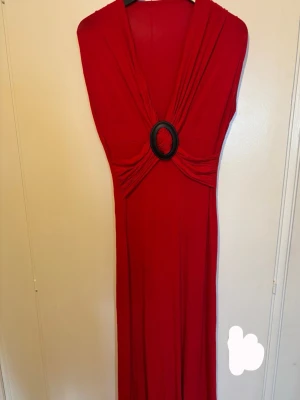 Röd långklänning  - Snygg röd långklänning köpt utomlands med djup v-ringning och en stor svart ringdetalj framtill och är ärmlös och är töjbart. 