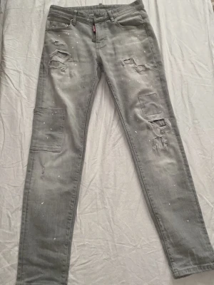 Grå cargobyxor med slitningar - Snygga grå cargobyxor med flera fickor på benen och coola slitningar samt färgstänk för en trendig look. Byxorna har raka ben och klassisk cargomodell. Perfekta för dig som gillar streetstyle och vill sticka ut lite extra.