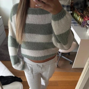 Randig stickad croppad tröja - Supermysig stickad tröja med breda gröna och vita ränder. Modellen är croppad med lång ärm och har en relaxed fit. Perfekt för lager-på-lager och chill dagar. Tröjan har ribbade muddar vid ärmslut och nederkant.