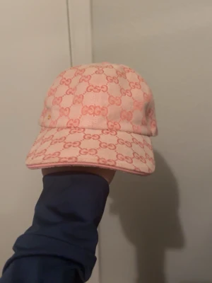 Rosa Gucci keps med GG-mönster - Säljer en snygg rosa keps från Gucci med det klassiska GG-mönstret i en ljus och mörkare rosa ton. Kepsen har böjd skärm och justerbar rem bak. Materialet känns som bomullscanvas och den har en liten gulddetalj på sidan. Perfekt för dig som vill sticka ut. Pris kan diskuteras.