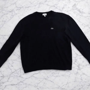 Svart tröja från Lacoste - Klassisk svart tröja från Lacoste med rund halsringning och diskret logotyp på bröstet. Tröjan har lång ärm och en enkel, stilren design som passar till det mesta. Perfekt för dig som gillar tidlös och clean stil.
