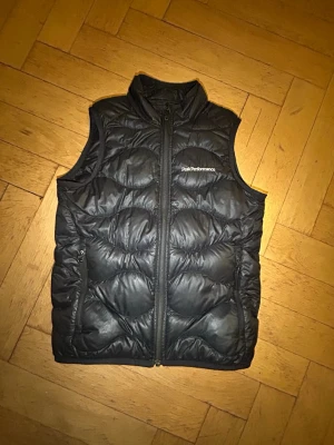  Peak Performance väst  - Snygg svart dunväst från Peak Performance.Västen har två sidofickor med dragkedja och ett quiltat mönster som ger en cool look. Perfekt för lager-på-lager-stil. 