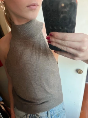 Brun ribbad polotopp ärmlös - Säljer en brun ärmlös polotopp med ribbad hög krage och bred ribbad kant nedtill. Toppen har en slim passform och är gjord i mjukt stickat material, perfekt att styla med jeans eller kjol.