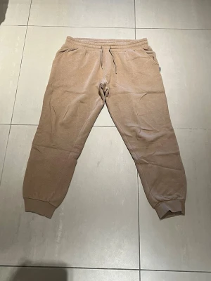 Beige mjukisbyxor Jack & Jones  - Säljer ett par beige mjukisbyxor med resår i midjan och justerbar dragsko. Byxorna har ribbade muddar vid bensluten och två sidofickor. Perfekta för chill dagar och riktigt sköna tack vare det mjuka materialet.