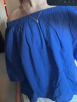 Blå offshoulder topp - Säljer en blå offshoulder topp med lös passform och trekvartsärm. Toppen har en elastisk kant upptill som gör att den sitter snyggt över axlarna. Perfekt för dig som vill ha en chill och trendig look. Rekomenderar till sommarn! 