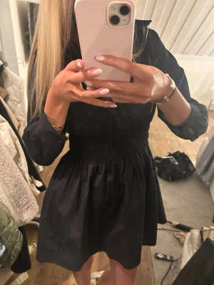 Svart kort klänning med v-ringning - Snygg svart kort klänning med v-ringning och trekvartslånga ärmar. Klänningen har markerad midja med smock och en lätt utställd kjol. Perfekt för dig som gillar en enkel men trendig look💕