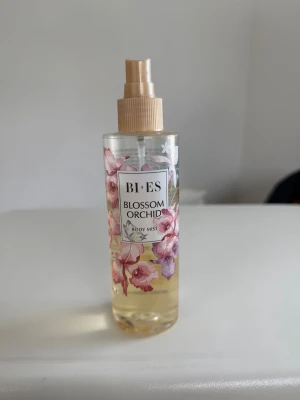 BI-ES Blossom Orchid Body Mist - Fräsch body mist från BI-ES med doften Blossom Orchid. Flaskan är genomskinlig med blommigt mönster i rosa och lila toner samt en beige spraykork. Innehållet är ljusgult och flaskan rymmer 200 ml. Perfekt för dig som gillar blommiga och fräscha dofter.