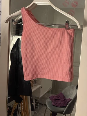 Rosa oneshoulder topp från Gina Tricot - Trendig rosa oneshoulder topp från Gina Tricot i ribbad bomullsmix. Croppad modell som passar perfekt till höga jeans eller kjol. Supersnygg och enkel att styla för en cool look.