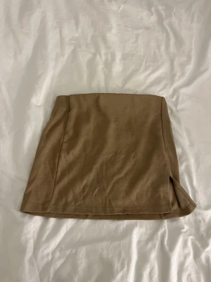 Beige kortkjol med slits - Stilren beige kortkjol i mjukt material med en liten slits på sidan för extra detalj. Kjolen är nästan aldrig använd och i mycket bra skicka !!