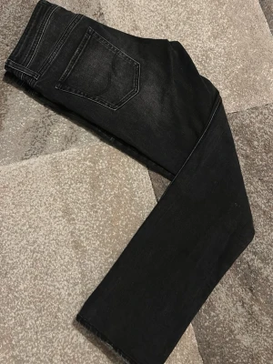 Svarta slim fit jeans från Jack & Jones - Svarta jeans från Jack & Jones med slim passform, modellen heter Slim Glenn. Jeansen har klassisk femficksdesign, svarta sömmar och lätt slitna detaljer framtill. Materialet är jeans med en mjuk känsla och stretch för extra komfort.