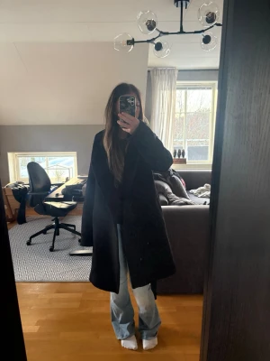 Svart lång kappa med stor luva - En svart, stilren och lång kappa med bred krage. Kappan har en ganska stor luva där bak och ett band runt midjan. På luvan har de förmodligen suttit knappar så de sitter lite trådar kvar, men nog lätt att ta bort! Använt typ 2 gånger. Kappan är i storlek xxs. Skriv för fler bilder💗pris går att diskutera 