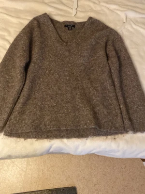Brun stickad tröja från Amisu - Mysig brun stickad tröja från Amisu med V-ringning och lång ärm. Tröjan har en lätt luddig yta och är tillverkad i ett mjukt material som passar perfekt för kyligare dagar. Enkel och stilren design som är lätt att matcha.