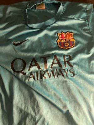 Barcelona Messi matchtröja turkos - Snygg turkos FC Barcelona matchtröja från Nike med Messi och nummer 10 på ryggen. Framsidan har klubbmärke, Nike-logga och Qatar Airways-tryck. Tillverkad i lätt och ventilerande material, perfekt för fotbollsträning eller att bära som supporter.