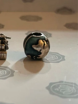 Pandora jordklot berlock - Säljer en rund silverpärla från Pandora med världskarta i relief. Pärlan har blå detaljer som symboliserar hav och silverfärgade kontinenter. Perfekt att addera till ditt armband för en personlig touch.