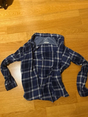 Blå rutig skjorta från Esentialls by Jack & Jones  - Snygg blå rutig skjorta från Esentialls by Jack & Jones med klassisk krage och långa ärmar. Skjortan har vita och grå rutor och knäppning framtill. Perfekt för en avslappnad och trendig stil. 