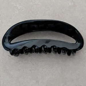 Svart hårklämma i plast - En enkel och stilren svart hårklämma med rundad form och starkt grepp. Perfekt för att snabbt sätta upp håret och hålla det på plats. Klämman har en blank finish och är tillverkad i tålig plast med klassisk design.