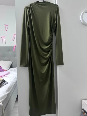 Olivgrön långklänning - H&M - Snygg olivgrön långklänning med lång ärm och draperad detalj längs sidan. Klänningen har en enkel, stilren design och är tillverkad i ett mjukt, stretchigt material som ger en smickrande passform.