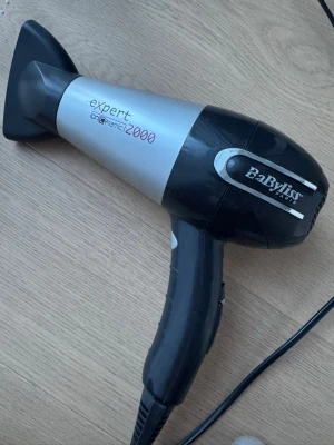BaByliss Expert hårfön svart/grå - BaByliss Expert Ion Ceramic 2000 hårfön i svart och grått med ergonomiskt handtag och justerbar värmeinställning. Utrustad med smalt munstycke för styling och keramisk jon-teknologi som motverkar frissigt hår. Perfekt för snabb och effektiv hårtorkning.