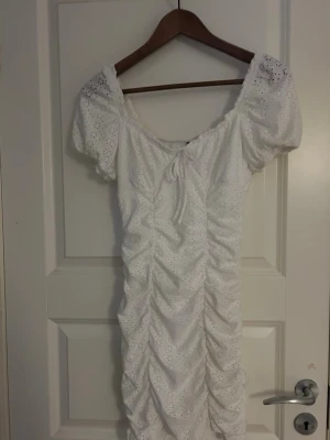 Vit kort klänning  - Supersöt vit kort klänning från H&M Divided i storlek XS. Klänningen har broderade detaljer och den stretchar ut sig när man har på sig den. Tillverkad i bomull med ett luftigt och fräscht uttryck, perfekt för varma dagar. Säljes då den inte längre kommer till användning.