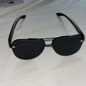 Svarta solglasögon från Maybach - Snygga svarta solglasögon från Maybach med rektangulära linser och diskreta gulddetaljer vid bågarna. Glasögonen har en stilren design med svarta skalmar där Maybach-loggan syns i guld. Perfekta för en trendig look.