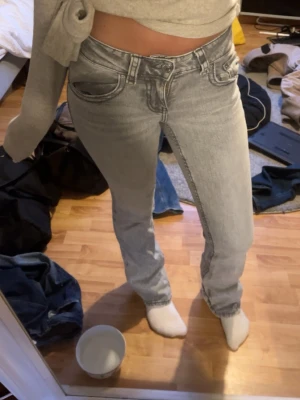 Ljusgrå bootcut - Säljer ett par ljusgrå jeans. Jeansen har klassisk femficksdesign och är tillverkade i ett mjukt denimtyg. Perfekta för en avslappnad och trendig look.