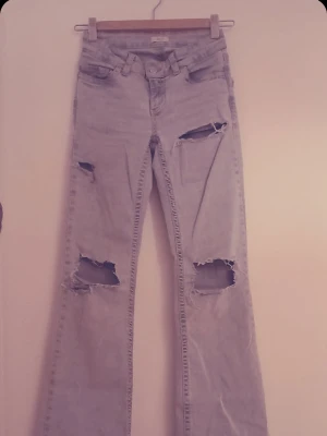 Ljusblå slitna bootcut jeans - Säljer ett par ljusblå bootcut jeans med flera stora slitningar och hål på benen. Jeansen har klassisk femficksdesign och hög midja. Perfekta för en avslappnad och trendig streetstil. Från Nelly har sprettat bort broderingen ibak på fickorna och dom har samt slitningar nere vid benen🙌 skriv om ni vill ha flera bilder på tillexempel.Dom har även några fläckar nere vid benen men inget som jag själv lägger märke till.