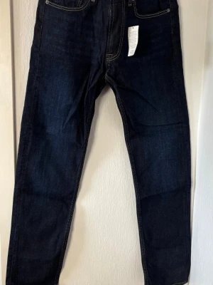 Mörkblå raka jeans - Snygga mörkblå jeans med rak passform och klassiska kontrastsömmar. Jeansen har fem fickor och är tillverkade i ett robust denimtyg som ger en tidlös look. Perfekta för dig som gillar enkel och stilren design.storlek 31x32 från dressmann