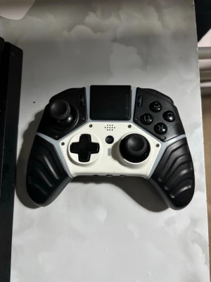 Svart och vit Nacon Revolution Pro - Säljer en Nacon Revolution Pro handkontroll i svart och vitt med ergonomiskt grepp, stora analoga spakar, styrkors och flera funktionsknappar. Kontrollern har en robust plastkonstruktion och text sopplade handtag för extra grepp. Perfekt för gaming på konsol.