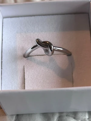 Silverfärgad ring med knutdetalj - Stilren ring i silverfärgad stål  metall med en snygg knutdetalj framtill. Ringen har en enkel och modern design som passar perfekt för dig som gillar minimalistiska accessoarer. Levereras i en vit ask.