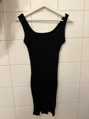 Svart ribbad klänning från SHEIN - Säljer en svart, ribbad kortklänning från SHEIN. Klänningen är ärmlös med breda axelband och har en kroppsnära passform. Perfekt för dig som gillar en enkel men stilren look. Materialet är stretchigt och bekvämt.