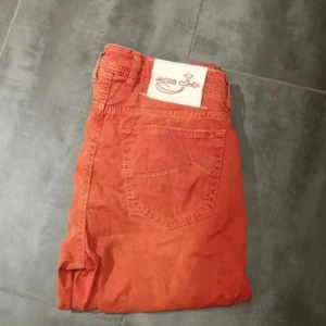 Röd byxor från Jacob Cohen - Snygga röda byxor från Jacob Cohen i storlek 33. Byxorna har en klassisk design med fem fickor och knappgylf. Perfekta för en snygg outfit. Passar mig som har 32-31 i midjan. Mycket snyggare än man tror men en skön korallvibe