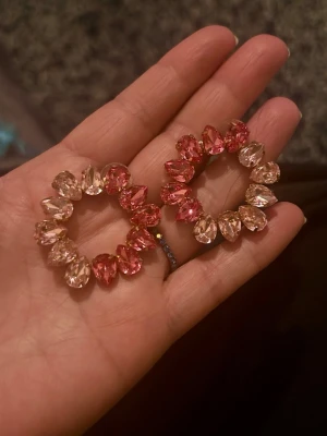 örhängen med kristaller  - Säljer ett par örhängen dekorerade med droppformade kristaller i rosa och ljusrosa nyanser. Örhängena har en glittrig och färgglad look som verkligen sticker ut. Perfekta för dig som vill ha något unikt och trendigt.liknar Caroline Svedbom örhängen 