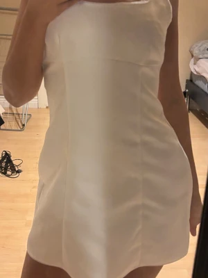 Vit kort klänning i satinlook från Zara - Säljer en stilren vit kort klänning med slät satinliknande yta och enkel, figurnära passform. Klänningen är i storlek s men för stor för mig för tappat vikt sitter tajt igentligen