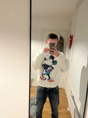 Vit Mickey Mouse hoodie Pull&Bear  - Vit hoodie från Pull&Bear med stort färgglatt Mickey Mouse-tryck på framsidan. Materialet är mjukt och bekvämt, perfekt för att chilla eller hänga med kompisar. Disney-design och klassisk passform, tillverkad i Portugal. Den passar M då den har blivit lite mindre i tvätten. 