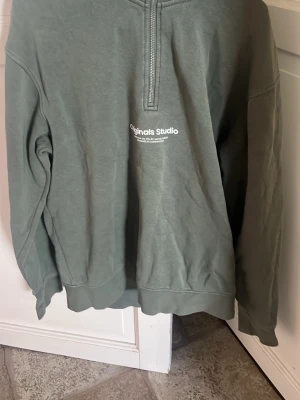 Grön halvzip sweatshirt Jack and Jones  - Snygg grön zipp hoddie från Jack and Jones  och tryckt logga på bröstet. Tröjan har en relaxed fit, ribbade muddar och är tillverkad i mjukt bomullsmaterial. Perfekt för en chill och stilren look. Säljer den för vuxit hur den, pris går diskutera!