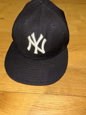 Svart New York Yankees keps - Klassisk svart keps från New Era med New York Yankees-logga broderad i vitt framtill. Kepsen har böjd skärm och ventilerande hål upptill. Materialet är tålig bomullstwill och baktill finns MLB-loggan broderad. Knappt ens rört den. 