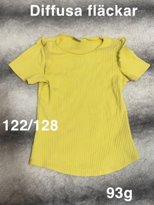 Gul ribbad topp med volangdetaljer - Snygg gul ribbad topp med korta ärmar och volangdetaljer vid axlarna. Perfekt för dig som gillar färg och vill ha en enkel men ändå unik topp i garderoben. Rund halsringning 🌸 Diffusa fläckar. Storlek 122-128