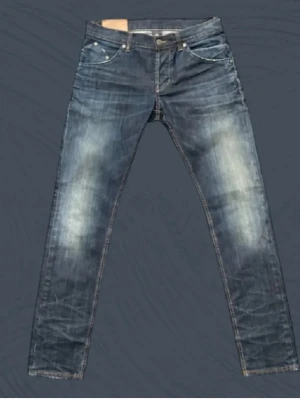 Blå slim fit jeans med slitningar - Snygga blå slim fit jeans med slitningar och ljusa tvättade partier på benen. Klassisk femficksmodell med knappgylf och kontrastsömmar. Perfekta för en avslappnad och trendig stil.