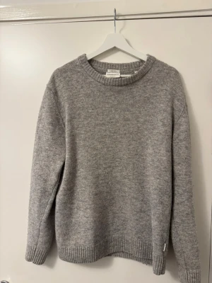 Grå stickad tröja från Lindbergh - Mysig grå stickad tröja från Lindbergh i mjuk ullblandning. Tröjan har rund halsringning, ribbade muddar vid ärmslut och nederkant samt en avslappnad passform. Perfekt för en vårdag eller som lager på lager under en kallare dag