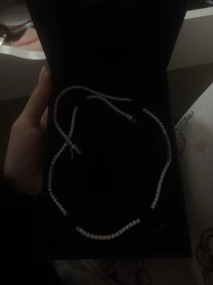 Glittrigt halsband med stenar - Säljer ett elegant halsband med gnistrande, klara stenar i rad som ger en lyxig känsla. Halsbandet har en klassisk, tunn design och är silverfärgat. Perfekt för dig som vill ha något som sticker ut och glänser lite extra. (aldrig använd, köpt för 1599)