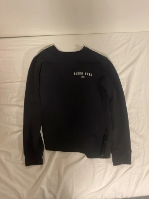 Svart sweatshirt från Björn Borg - En stilren svart sweatshirt från Björn Borg med tryck 'BJÖRN BORG 1956' på bröstet. Tröjan har rund halsringning och långa ärmar. Perfekt för en avslappnad och sportig look. I väldigt bra skick inga fläckar osv. 