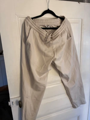 Beige mjukisbyxor med dragsko Cubus - Snygga beige mjukisbyxor med bred resår i midjan och dragsko för perfekt passform från Cubus. Byxorna har avslappnad passform och är tillverkade i mjukt material som känns skönt mot huden. Perfekta för chill dagar hemma eller när du vill vara bekväm.