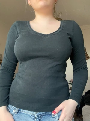 Mörk grön långärmad topp  - En mörk grön långärmad topp med v-ringning och figurnära passform. Toppen är enkel och stilren, perfekt att matcha med jeans eller kjol. Materialet känns mjukt och stretchigt, vilket gör den bekväm att bära hela dagen. Lite urtvättad. Väldigt fin passform!