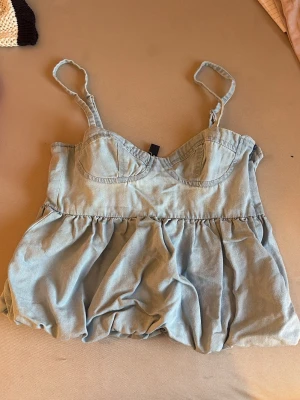 Ljusblå jeans topp från H&M Divided - Supersöt ljusblå jeanstopp från H&M Divided med tunna axelband och markerad byst. Toppen har en luftig och lätt form, perfekt för varma dagar. Tillverkad i mjukt bomullsmaterial som känns skönt mot huden.