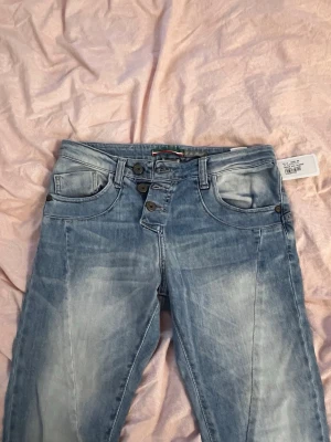 Ljusblå jeans med knappar X X Small - Säljer ett par ljusblå jeans från X X Small med snygg tvätt och flera knappar i gylfen. Jeansen har klassisk femficksdesign och raka ben. Perfekta för dig som gillar en avslappnad och trendig stil. Jeansen är vintage med prislapp kvar. Nypris 1600kr 