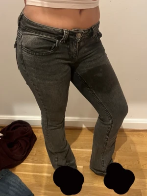 Grå bootcut jeans med låg midja - Säljer ett par grå bootcut jeans med låg midja och klassiska fem fickor. Jeansen har snygga sömdetaljer och knappar på bakfickorna.