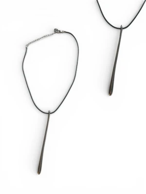 Svart halsband med metallhänge - Stilrent halsband med svart läderrem och ett långt, droppformat hänge i mörk metall. Hänget har en minimalistisk design och halsbandet stängs med ett justerbart kedjelås. Perfekt för dig som gillar enkel men cool stil.