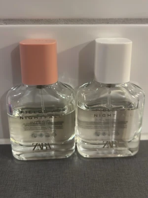 ZARA Fields at Nightfall parfymduo - Två parfymer från ZARA, Fields at Nightfall och Fields at Nightfall Intense. Flaskorna är genomskinliga med en stilren design, en har vit kork och den andra har en matt rosa kork. Båda har minimalistisk text på framsidan och innehåller klar vätska.